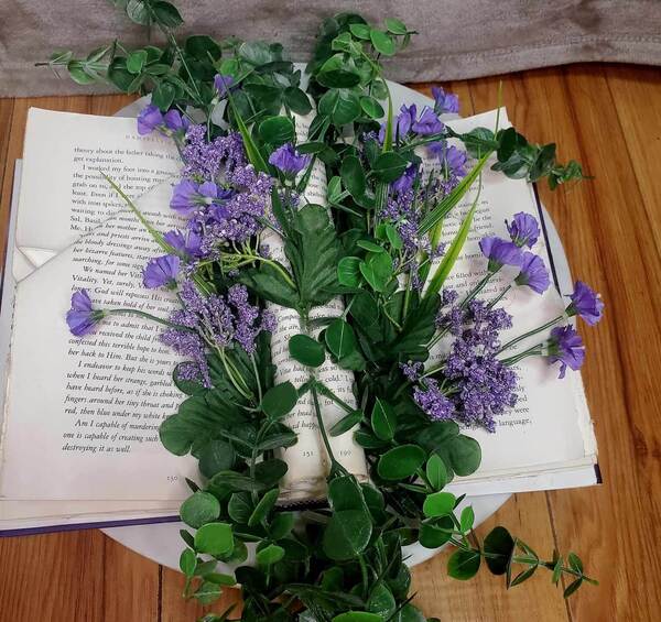 Many small purple flowers appear to grow with foliage throughout the folded pages of a book.