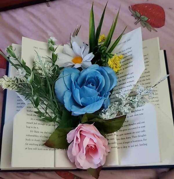 Pink and blue roses sit with foliage in the center of a book with folded pages.