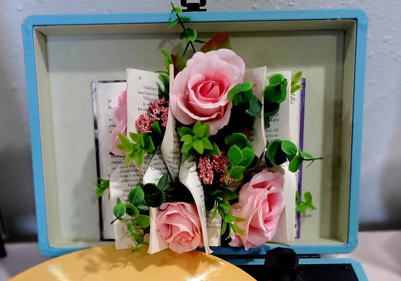 Book with folded pages and pink roses arranged throughout the folds. The book is sitting atop a modern looking record player.