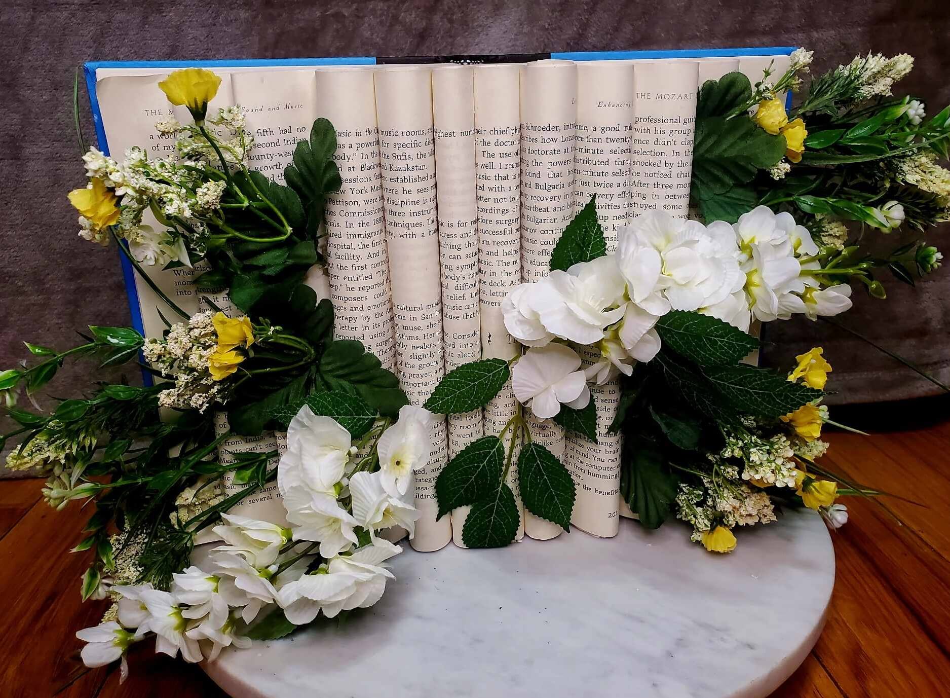 Book with folded pages arranged with small white and yellow flowers.